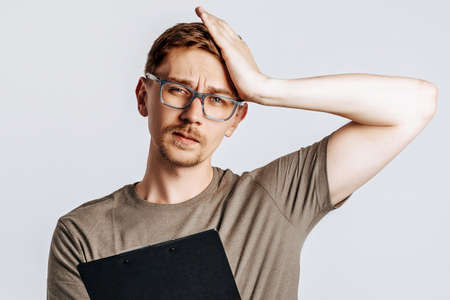 Young handsome man in glasses holding folder for papers with documents, student, worker looks data information, posing for photo isolated on gray background.の写真素材