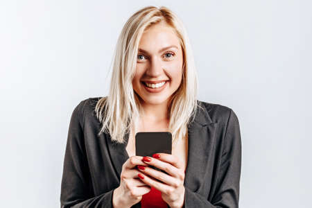 Beautiful young cute girl smiling and holding phone on gray isolated backgroundの写真素材