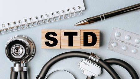 Wooden block form the word STD with stethoscope, pills, notepad, pen on the doctor's desktop. Medical concept.の写真素材