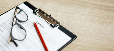 A contract on a wooden work table with glasses and a red pencil. The documents are ready for...
