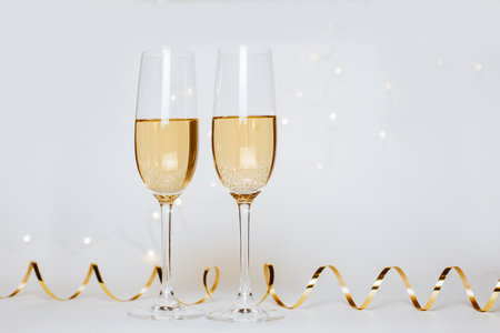 Two glasses of champagne with lights and ribbons on a white background holidayの写真素材