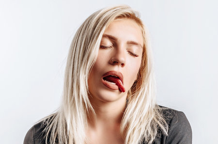 Beautiful young girl unhappy and tired showing tongue on gray isolated backgroundの写真素材