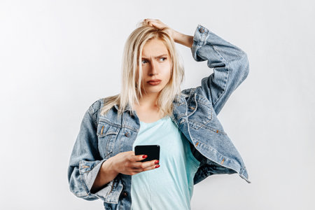 Beautiful young girl unhappy and holding phone on gray isolated backgroundの写真素材