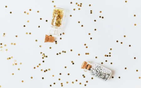 Spangles of gold and silver are scattered from bottles on a white backgroundの写真素材