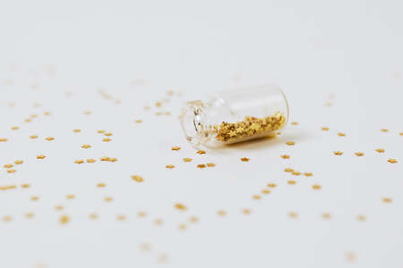 Spangles of gold and silver are scattered from bottles on a white backgroundの写真素材