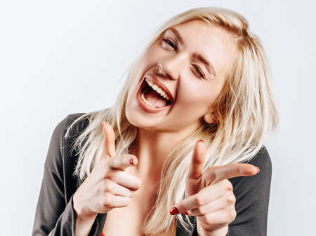 Beautiful young girl fooling around and pointing fingers at screen on gray isolated backgroundの写真素材