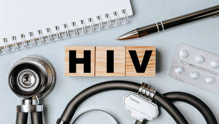 Wooden block form the word HIV with stethoscope, pills, notepad, pen on the doctor's desktop. Medical concept.の写真素材