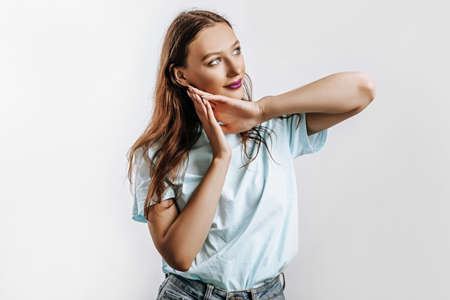 A beautiful young girl smiles, dreams and holds her hands near her face on a white isolated gray background. Place for advertising. Positive woman with fashion make-up with purple lips.の写真素材