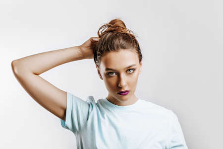 A beautiful brunette girl holds her hair and makes her own hairstyle. Young model with long hair, fashion makeup with purple lips on an gray background. The woman seriously looking at the camera.の写真素材