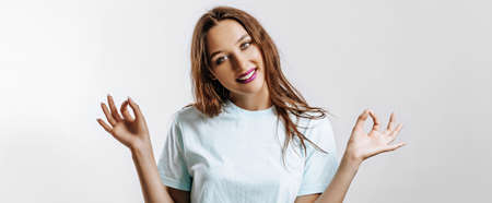 All OK. A beautiful young girl smiles and shows with two hands the ok sign from the fingers. on a gray background. Place for advertising. Positive woman with fashion make-up with purple lips.の写真素材