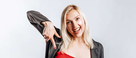 Beautiful young girl pointing fingers down on gray isolated backgroundの写真素材