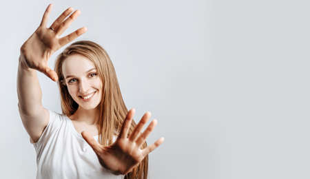 Young beautiful girl smiling and pulling her hands towards camera on gray isolated backgroundの写真素材