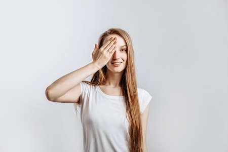 Young beautiful girl smiling and covering half of her face with hand on gray isolated backgroundの写真素材