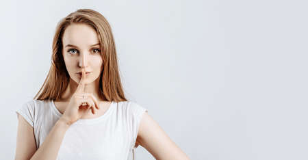Young beautiful girl smiling and showing finger hush gesture on gray isolated backgroundの写真素材