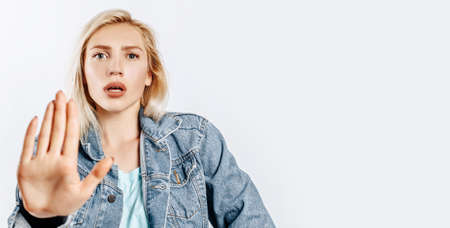 Beautiful young girl unhappy frown and says stop with a hand gesture on gray isolated background