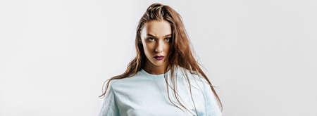 Beautiful young brunette girl with green eyes with long hair with fashion makeup with purple lips on an isolated gray background. The woman frowning and seriously looking at the camera. Evil modelの写真素材