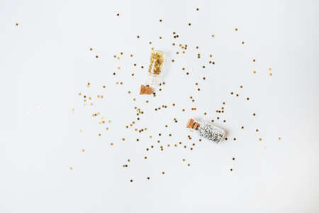 Spangles of gold and silver are scattered from bottles on a white background