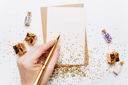 Girl writing blank note with gifts, pen and gold glitter stars on white background
