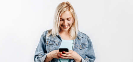 Beautiful young cute girl smiling and looking at phone on gray isolated background