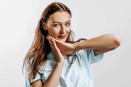 A beautiful young girl smiles, dreams and holds her hands near her face on a white isolated gray background. Place for advertising. Positive woman with fashion make-up with purple lips.の写真素材