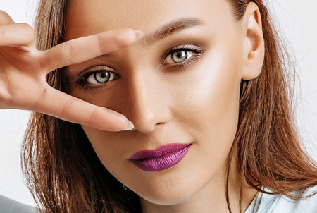 Hey smile you. Portrait of cute glamor girl brunette woman with fashion make-up purple lips winking happily showing peace victory gesture as fooling around, being optimistic. Beautiful female face.の写真素材