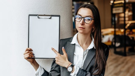 The woman shows information on the tablet. Place for advertising. Business concept. The girl in glasses holds the documents and explains the information. White blank sheet of paper.の写真素材