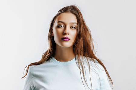 Beautiful young brunette girl with green eyes with long hair with fashion makeup with purple lips on an isolated gray background. The woman seriously looking at the camera. Kind cute modelの写真素材
