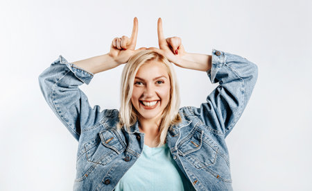 Beautiful young cute girl smiling fooling around and making horns gesture on gray isolated backgroundの写真素材
