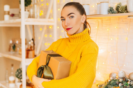 Beautiful cheerful happy young girl with christmas gifts on the background of the new year kitchenの写真素材