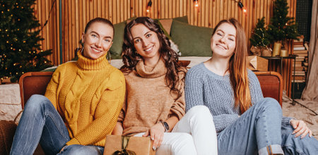 Three beautiful cheerful happy young girls girlfriend give Christmas gifts on the background of a new year tree at homeの写真素材