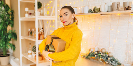 Beautiful cheerful happy young girl with christmas gifts on the background of the new year kitchenの写真素材
