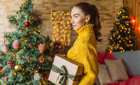 Beautiful cheerful happy young girl with christmas gifts on the background of a new year tree at homeの写真素材