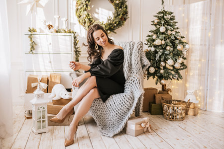 Beautiful cheerful happy young girl with christmas gifts on sofa on the background of a new year tree at homeの写真素材