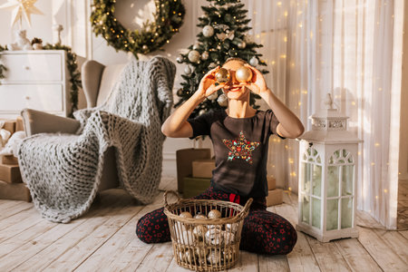 Beautiful cheerful happy young girl on the floor in pajamas with christmas toys near the new year tree at homeの写真素材