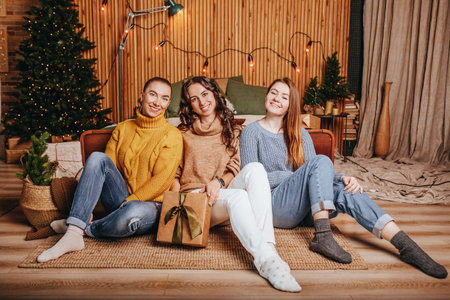 Three beautiful cheerful happy young girls girlfriend give Christmas gifts on the background of a new year tree at homeの写真素材