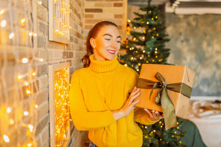 Beautiful cheerful happy young girl with christmas gifts on the background of a new year tree at homeの写真素材