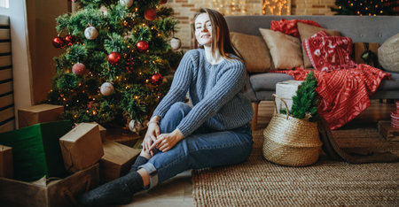 Beautiful cheerful happy young girl with christmas gifts on the floor near the new year tree at homeの写真素材