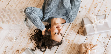 Beautiful cheerful happy young girl with christmas toys and gifts on wooden floorの写真素材