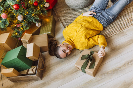 Beautiful cheerful happy young girl with christmas gifts on the background of a new year tree at homeの写真素材
