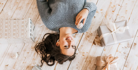 Beautiful cheerful happy young girl with christmas toys and gifts on wooden floorの写真素材