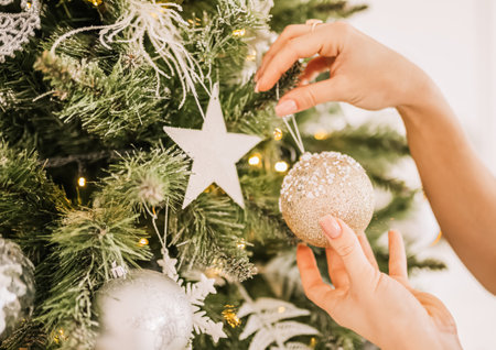 Beautiful cheerful happy young girl decorate new year tree christmas toys at homeの写真素材