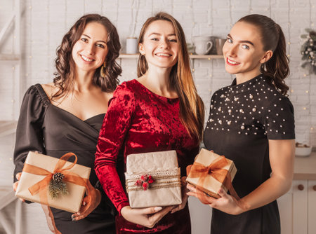 Three beautiful cheerful happy young girls friend laughing with gift at the christmas dining table on the background of the new year kitchenの写真素材