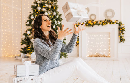 Beautiful cheerful happy young girl with christmas gifts on the background of a new year tree at homeの写真素材