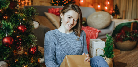 Beautiful cheerful happy young girl with christmas gifts on the floor near the new year tree at homeの写真素材