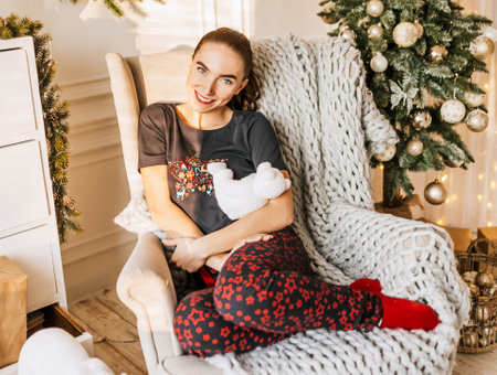 Beautiful cheerful happy young girl with christmas gifts on sofa on the background of a new year tree at homeの写真素材