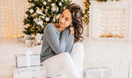 Beautiful cheerful happy young girl with christmas gifts on the background of a new year tree at homeの写真素材