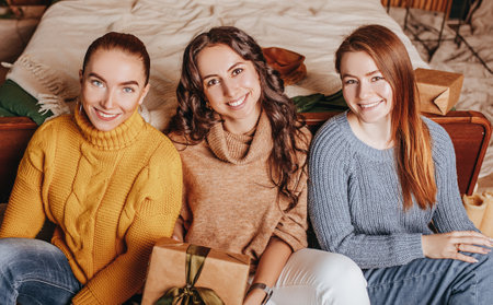 Three beautiful cheerful happy young girls girlfriend give Christmas gifts on the background of a new year tree at homeの写真素材