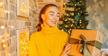 Beautiful cheerful happy young girl with christmas gifts on the background of a new year tree at homeの写真素材