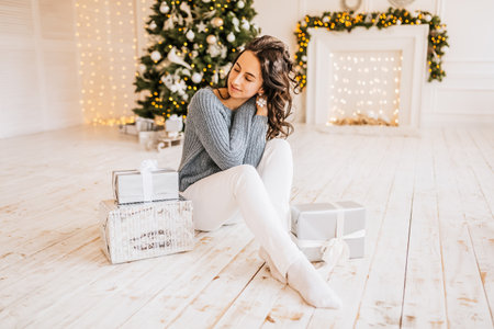 Beautiful cheerful happy young girl with christmas gifts on the background of a new year tree at homeの写真素材