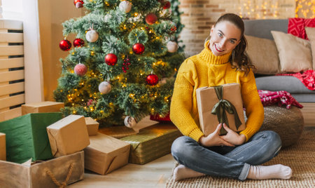 Beautiful cheerful happy young girl with christmas gifts on the background of a new year tree at homeの写真素材